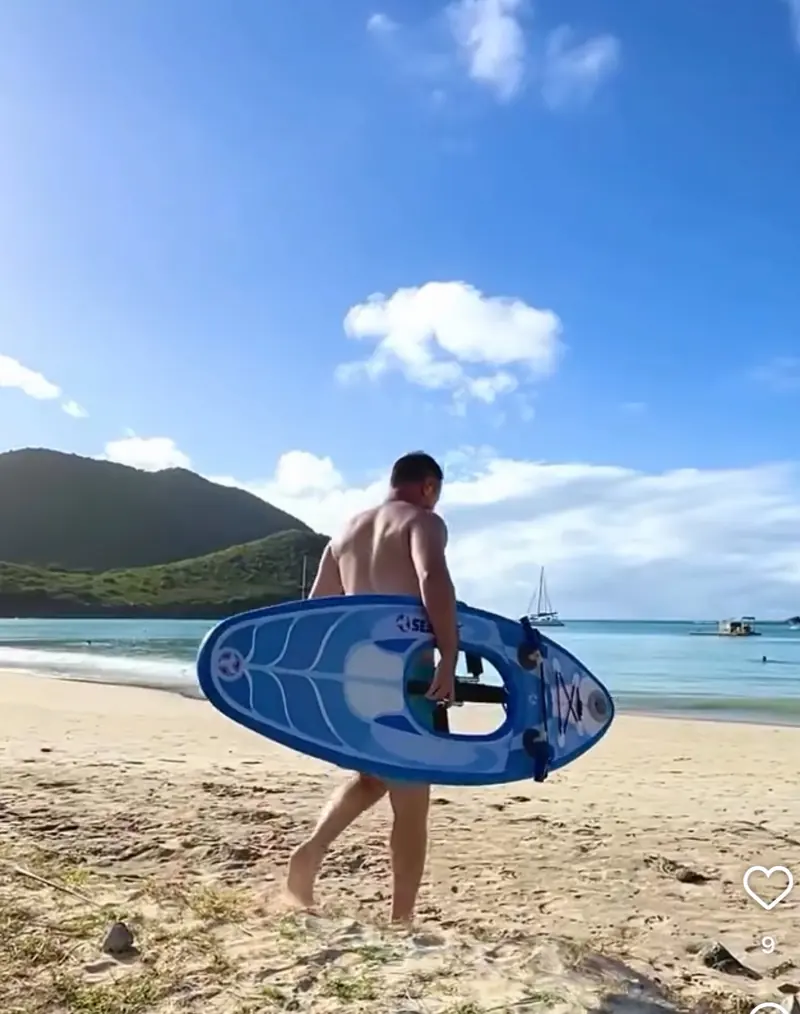 Maui Sea Board electric snorkeling board floating in clear shallow turquoise water on a Maui beach, with golden sand and green mountains in the distance