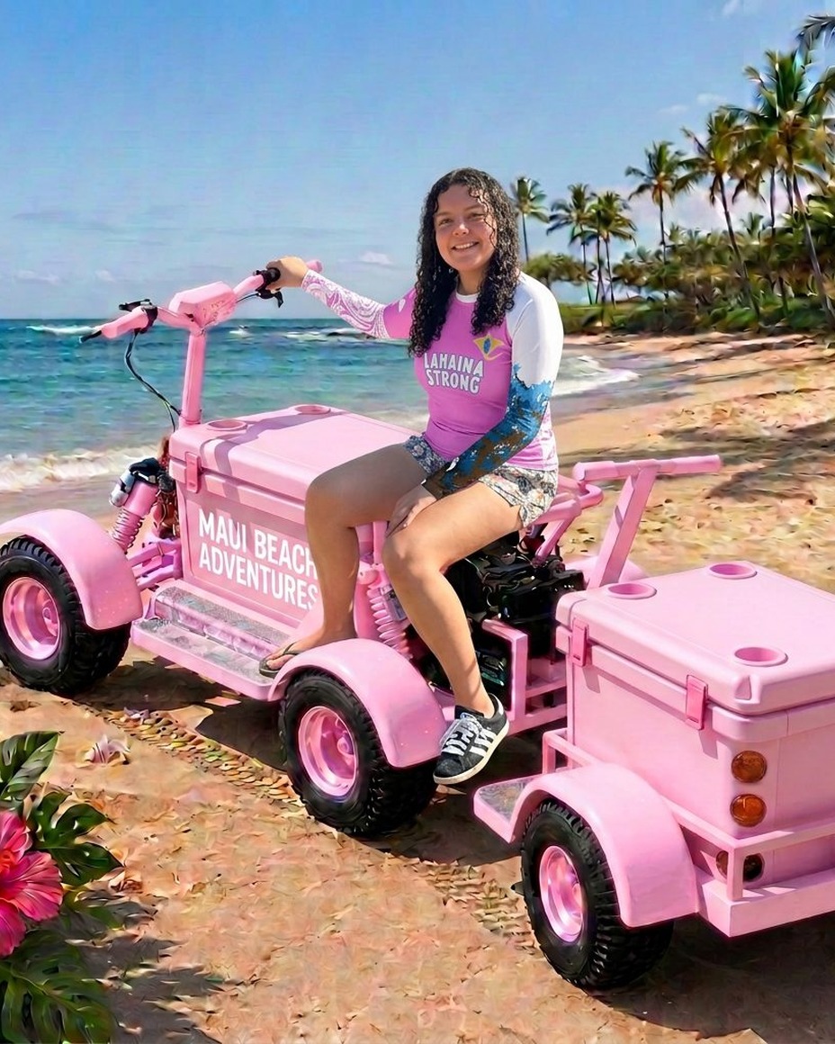 Bella in a pink Lahaina Strong rashguard beside a loaded pink Maui Beach Adventures beach cart with cooler, chairs and canopy set up on the sand