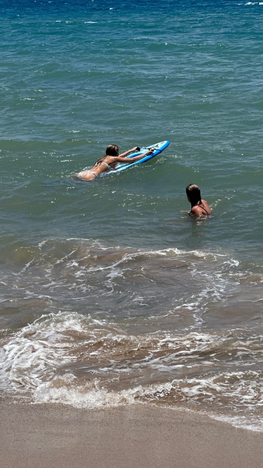 Two riders on Maui Sea Board snorkeling boards riding through light shore break just off a sunny Maui beach