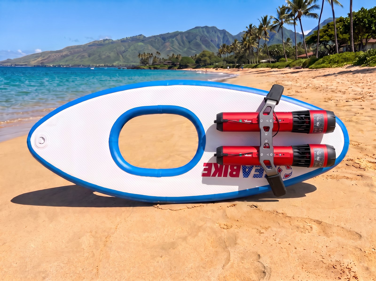 White and blue Maui Sea Board electric snorkeling board on golden Maui beach sand with twin red Waydoo Subnado motors mounted lengthwise on the top deck, joined by a gray twin-engine bracket, turquoise ocean and green West Maui mountains behind